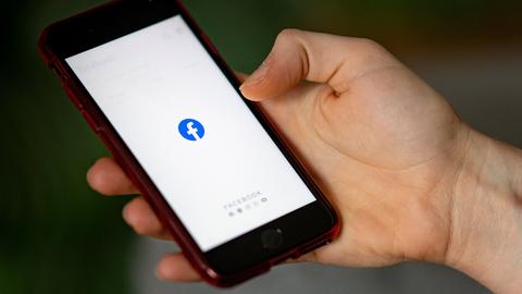 Hand hält ein Smartphone mit einem Facebook-Symbol auf dem Display