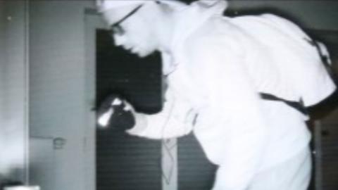 Ein Einbrecher ist auf dem schwarz-weißen Bild einer Überwachungskamera in einer Wohnung zu sehen.