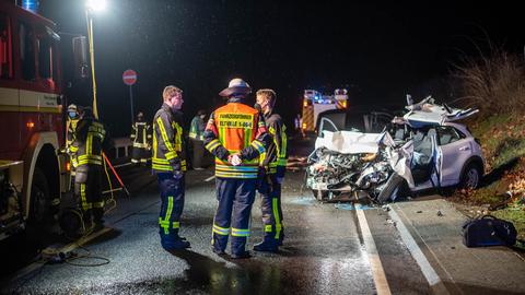 Feuerwehrleute neben einem Unfallauto.