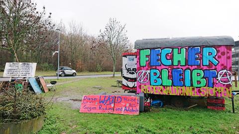 Auf einer Grünfläche steht ein Bauwagen, auf dem steht "Fecher bleibt, Riederwaldtunnel stoppen"