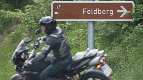 Motorradfahrer unscharf im Bildvordergrund, Straßenschild mit der Aufschrift "Feldberg" scharf im Bildhintergrund.