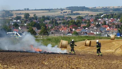 Auf einem Feld brennt Stroh, zwei Feuerwehrleute löschen den Brand.