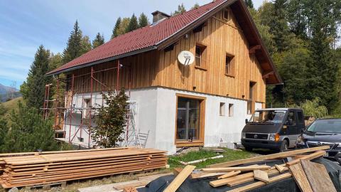 Ein Haus mit Holzverkleidung und Gerüst an der Seite - in bewaldeter Umgebung.