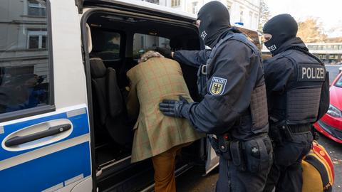 Polizisten schieben Festgenommmenen in ein Polizeiauto