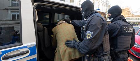 Polizisten schieben Festgenommmenen in ein Polizeiauto