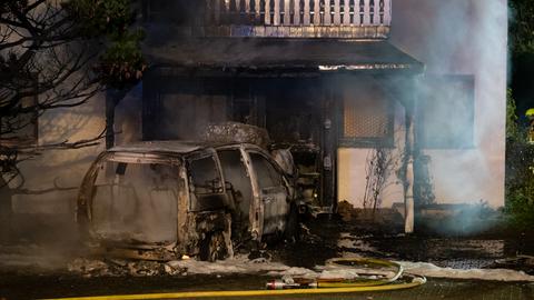 Ein ausgebranntes Auto vor einem Mehrfamilienhaus, der Eingangsbereich ist stark beschädigt.