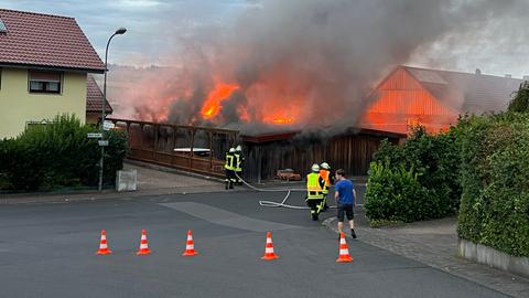 Eine Werkstatt steht lichterloh in Flammen - davor Feuerwehrleute. 