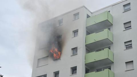 Aus einem Fenster eines Mehrfamilienhauses schlagen Flammen und Rauch.