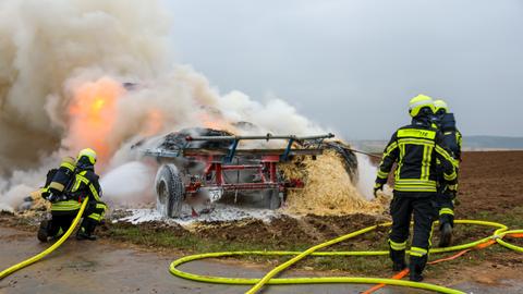 Brennende Strohballen auf einem Feld, die Feuerwehr löscht.