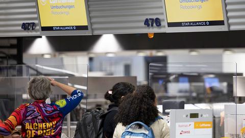 Passagiere schauen vor Schaltern stehend auf die Anzeigetafeln, auf denen "Umbuchungen" steht.