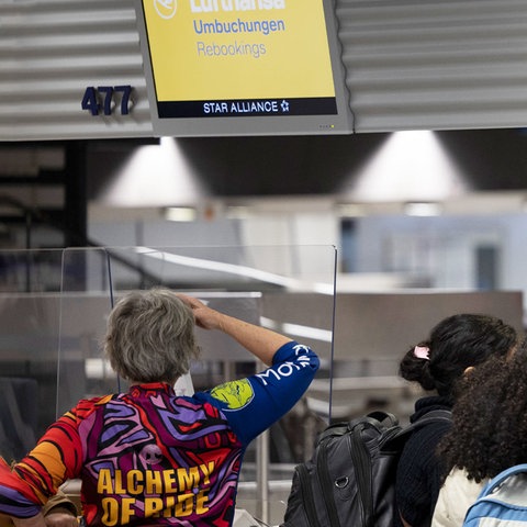 Passagiere schauen vor Schaltern stehend auf die Anzeigetafeln, auf denen "Umbuchungen" steht.
