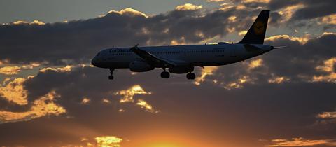 Ein Flugzeug im Landeanflug vor einem Sonnenuntergang und Wolken.