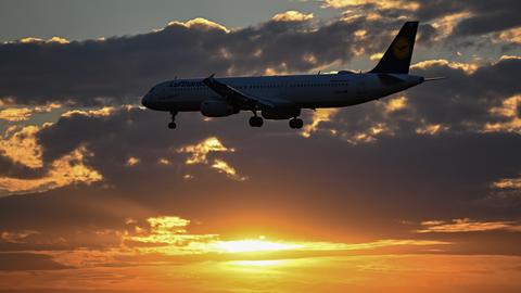 Ein Flugzeug im Landeanflug vor einem Sonnenuntergang und Wolken.