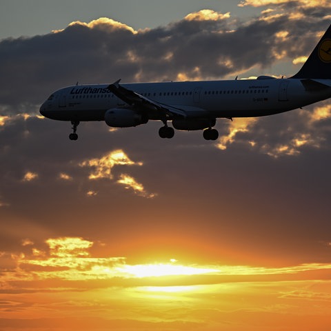 Ein Flugzeug im Landeanflug vor einem Sonnenuntergang und Wolken.