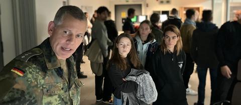 Zwei junge Frauen stehen neben einem Soldaten und lassen sich etwas erklären