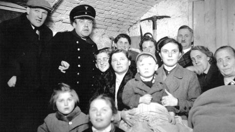 Erwachsene und Kinder sitzen dicht zusammengedrängt in einem Luftschutzkeller