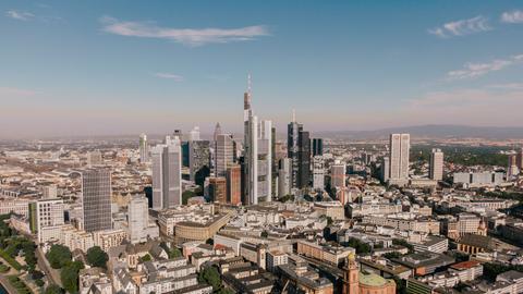 Die Skyline Frankfurts im Vordergrund, im Hintergrund Wohnhäuser und der Taunus.  
