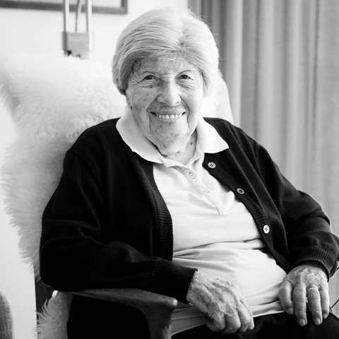 Trude Simonsohn sitzt in einem Sessel und lächelt in die Kamera. Das Foto ist in schwarz-weiß gehalten.