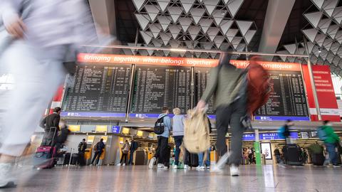 Menschen stehen zu den Osterferien vor einer Anzeigetafel im Flughafen Frankfurt. 