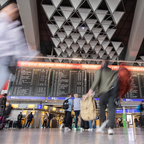 Menschen stehen zu den Osterferien vor einer Anzeigetafel im Flughafen Frankfurt. 