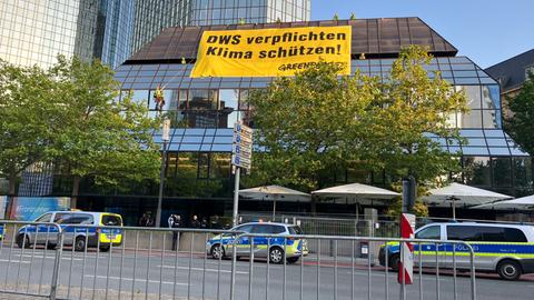 Banner mit "Klima schützen" an einem Gebäude mit Hochhaus im Hintergrund