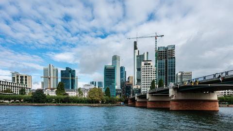 Brücke über den Main, dahinter ein Teil der Frankfurter Skyline bei schönem Wetter