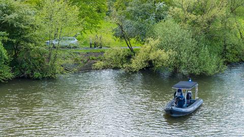 Boot der Wasserschutzpolizei auf einem Fluss, Auto und Polizisten am dicht bewachsenen Ufer