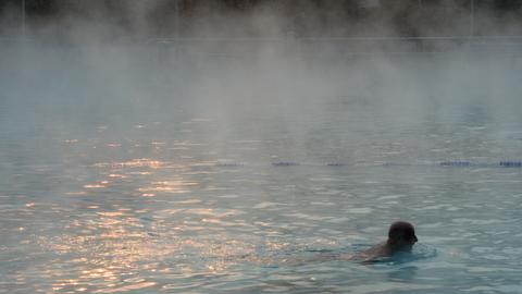 Ein Mann schwimmt in einem Schwimmbecken, aus dem Dampf aufsteigt