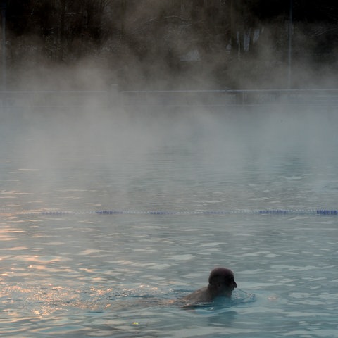 Ein Mann schwimmt in einem Schwimmbecken, aus dem Dampf aufsteigt