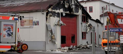 Halle, von der nach einem Brand rußige Teile abgefallen sind, zwei Feuerwehrwagen davor