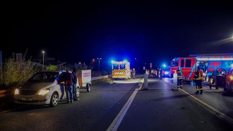 Feuerwehrautos und ein Rettungswagen stehen auf einer dunklen Bundesstraße, im Vordergrund ein weißes Auto am Straßenrand.
