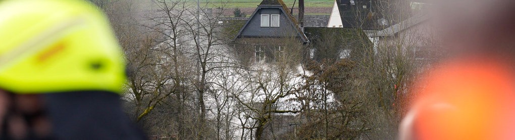 In der Ferne hinter Bäumen weißer Rauch, im Vordergrund sind Feuerwehrleute zu sehen.