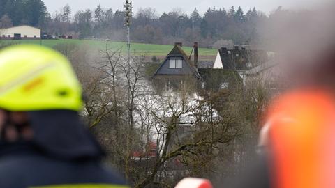 In der Ferne hinter Bäumen weißer Rauch, im Vordergrund sind Feuerwehrleute zu sehen.