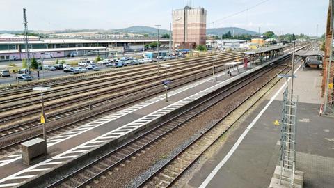 Blick von oben über den Bahnhof. Es sind Gleise, Bahnsteige und ein vollgeparkter Parkplatz neben dem Bahnhof zu sehen.