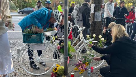 Fahrrad an Laternenpfahl, davor Blumen und Grablichter.