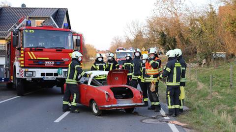 Ein roter Oldtimer steht quer auf der Fahrbahn, dahinter ein Feuerwehrauto.
