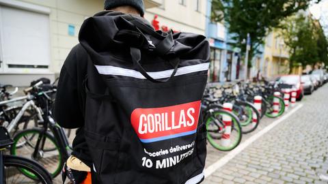 Ein Gorillas-Fahrer trägt einen Rucksack und steht vor seinem Fahrrad.