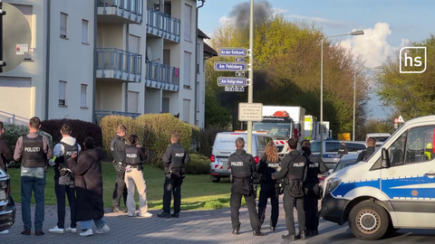 Polizeibeamte stehen vor einem Haus, über dem eine Rauchwolke aufsteigt.