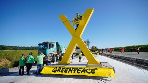 Ein mehrere Meter hohes gelbes X steht auf der Fahrbahn vor einem Baufahrzeug. 