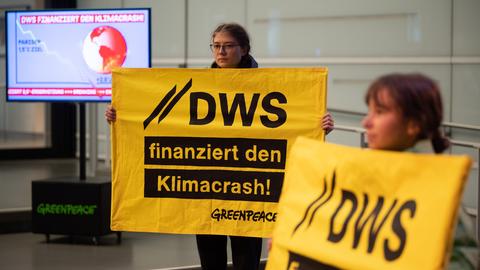 Demonstrierende halten während einer Protestaktion der Umweltschutzorganisation Greenpeace vor dem Eingang des Vermögensverwalters DWS Schilder mit der Aufschrift "DWS finanziert den Klimacrash!" hoch.