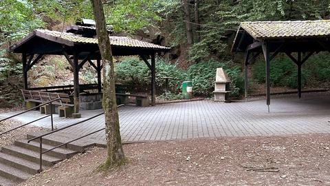 Zwei Holzunterstände im Wald, ein gemauerter Grill steht in der Mitte.