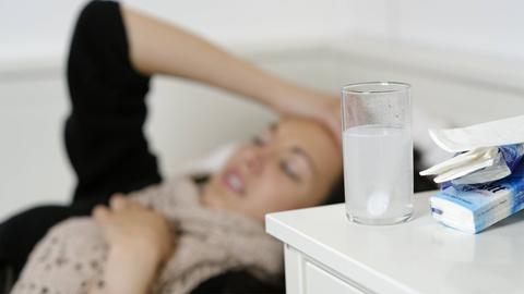 Eine junge Frau liegt mit einer Grippe im Bett.