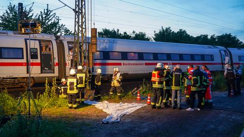 Das Bild zeigt Einsatzkräfte der Feuerwehr und Polizei in der Dämmerung. Sie stehen auf einem Feld vor einem weiß-roten ICE, der wegen eines Oberleitungsschadens ohne Strom war und liegen geblieben ist.