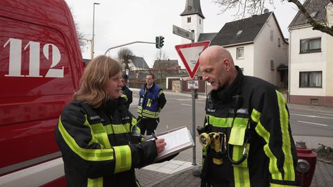 Feuerwehrleute stehen vor einem Einsatzauto und schreiben in einen Block.