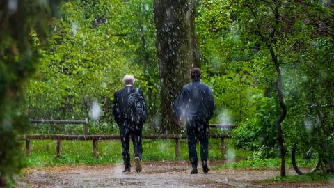 Zwei Männer laufen durch einen Graupelschauer in einem Park.