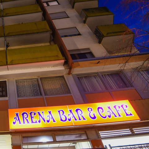 Leuchtschild "Arena Bar & Cafe" im Erdgeschoss eines Hochhauses.