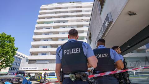 Foto: Drei Polizisten stehen neben einem Absperrband vor einem Hochhaus.