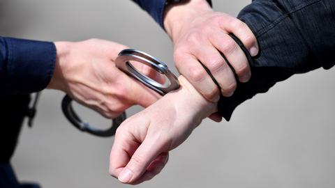 Hände, die mit Handschellen andere Hände "festnehmen".