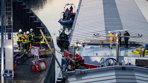 Das Bild zeigt ein havariertes Schiff in der Mainschleuse in Mühlheim (Offenbach). Einsatzrkäfte der Feuerwehr sind auf dem Frachter und in Schlauchbooten auf dem Wasser mit der Bergung befasst.