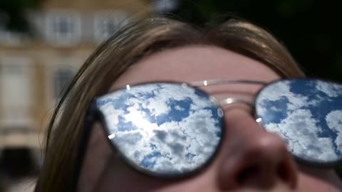 Der Himmel mit lockeren Wolken spiegelt sich in der Sonnenbrille einer Frau